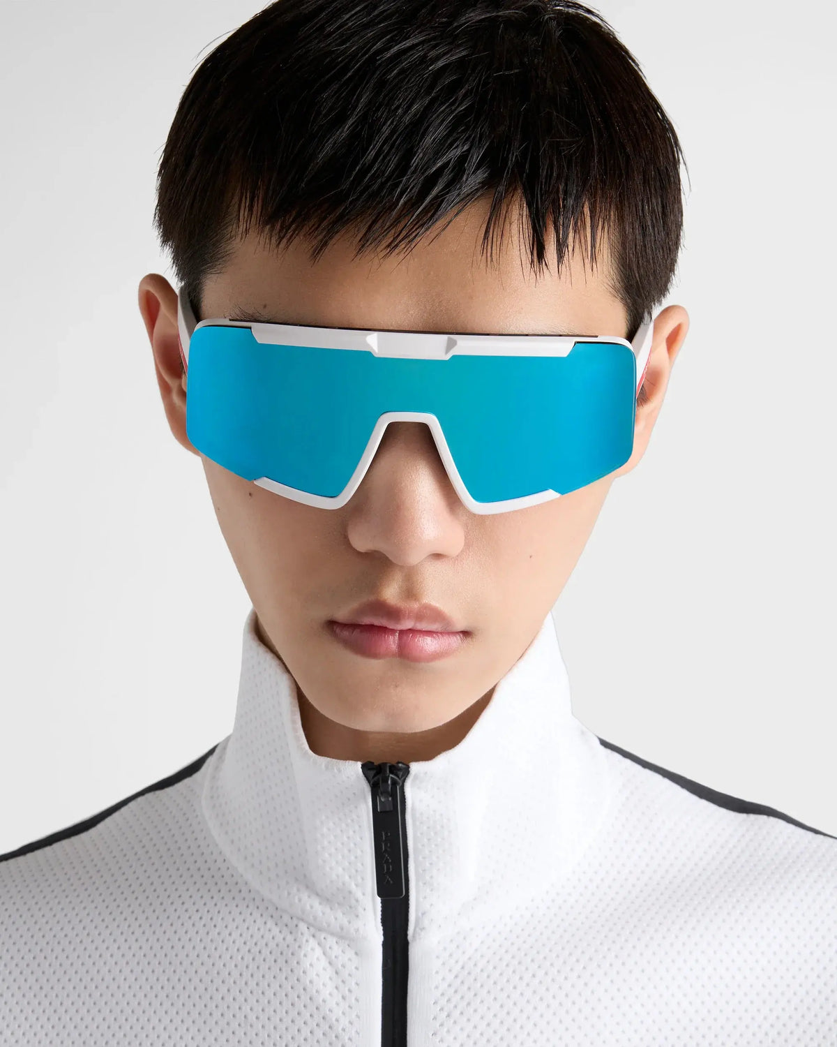 Homme portant des lunettes de sport bleues sur un maillot blanc perforé.